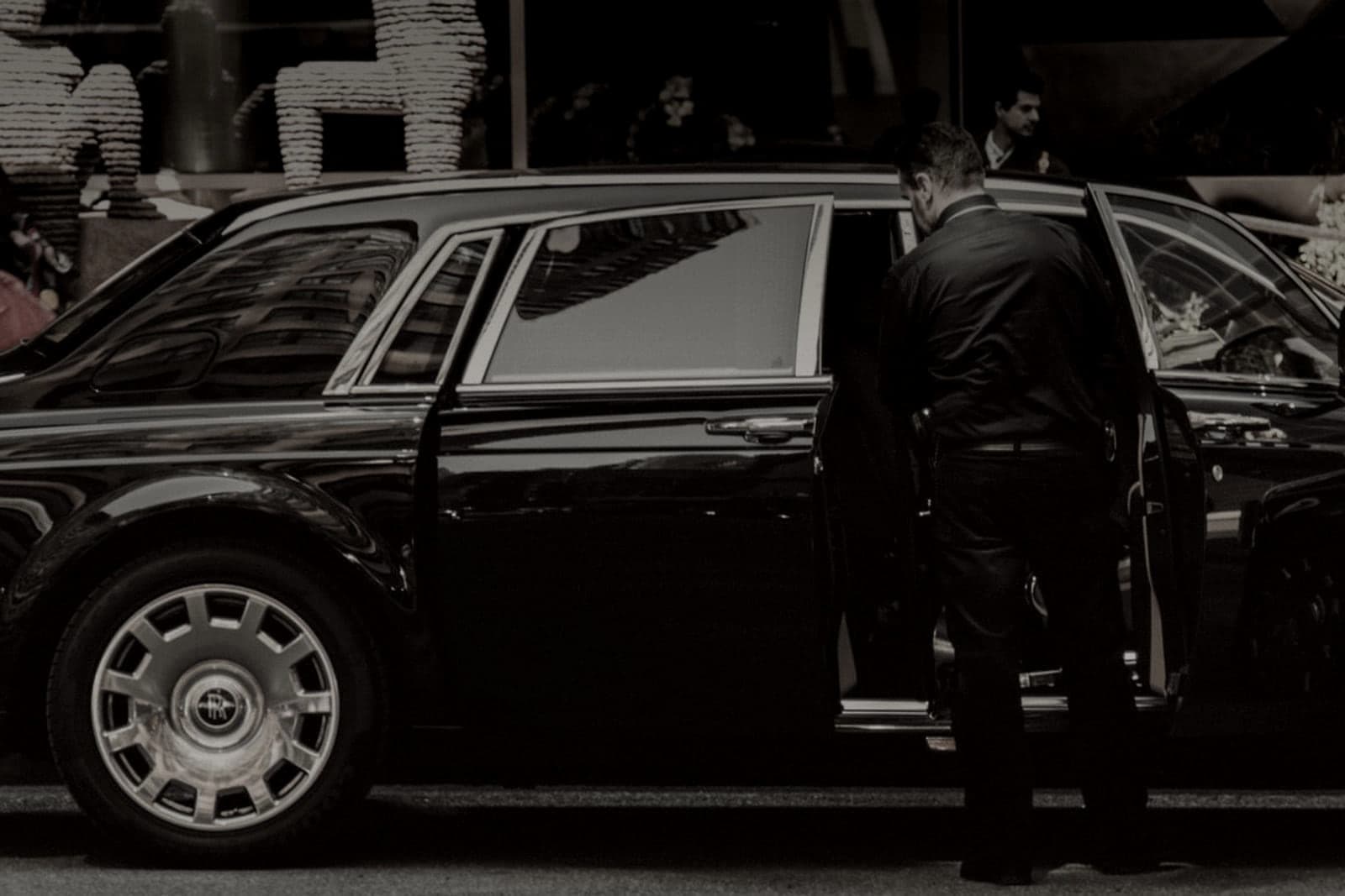 Chauffeur holding the rear door open beside a black car at a venue entrance